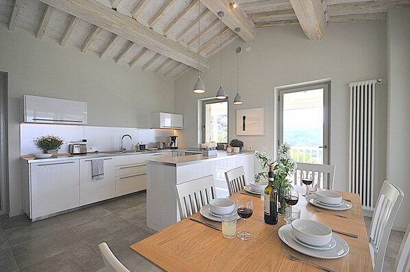 Una cocina moderna con armarios blancos, una mesa de comedor de madera para dos personas y vista al mar a través de un ventanal grande.