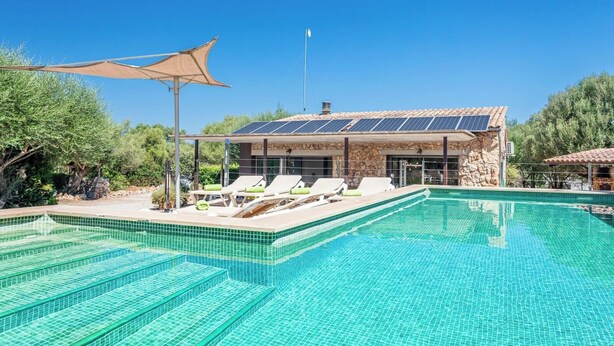 Ein Swimmingpool mit Liegestühlen, ein überdachter Bereich mit Sonnenschutz und ein Gebäude mit Solaranlage.