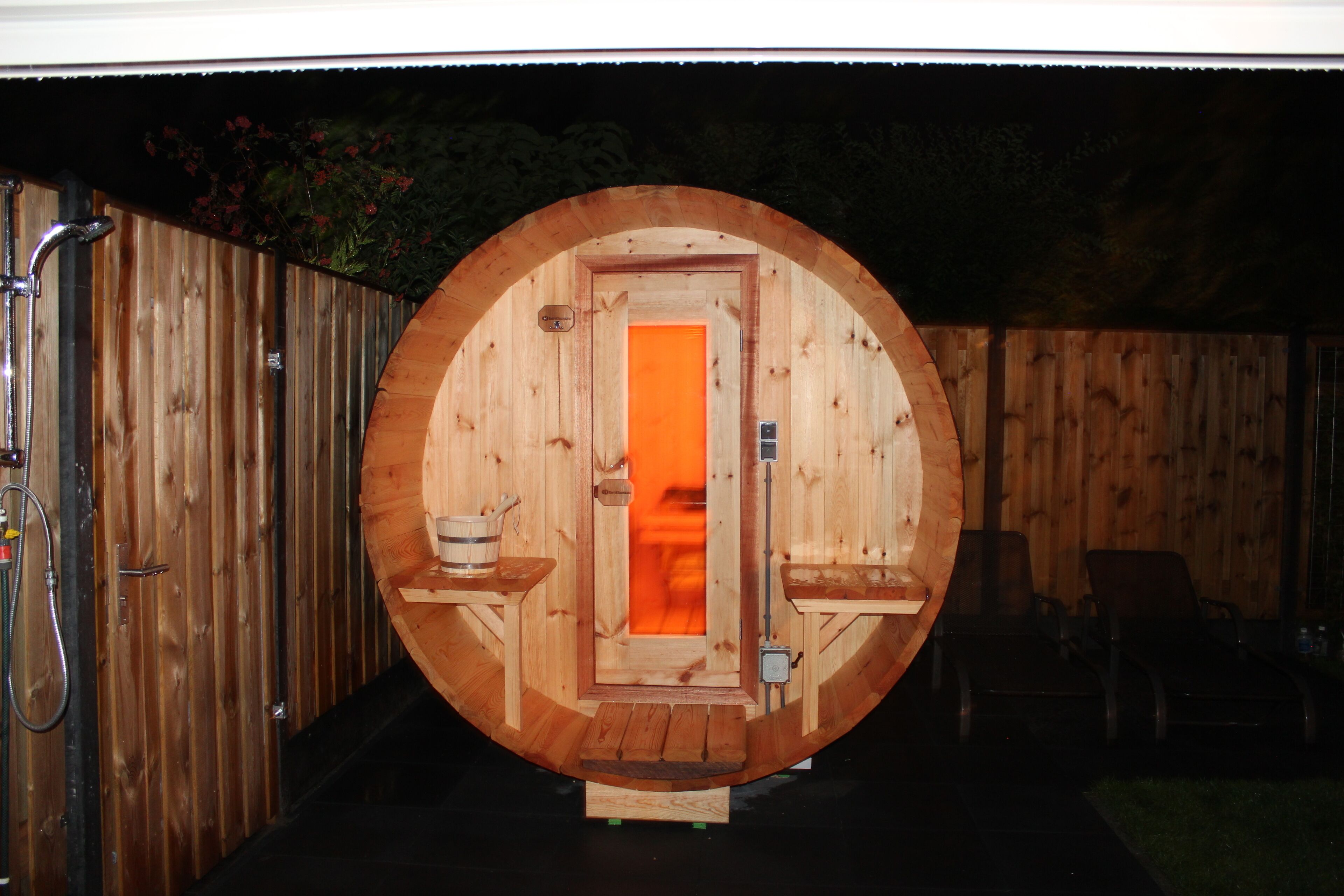 Een houten sauna met een ronde deur, een bank en een kleine tafel met een emmer.