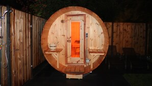 A wooden sauna with a circular door, a bench, and a small table with a bucket.