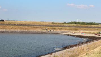 Een kustgebied met een zandstrand, een rustig waterlichaam en windturbines in de verte.