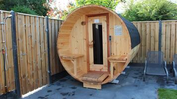 Een houten sauna met een deur, een klein bankje en een bankje buiten.