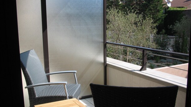 En balkon med udsigt over en have og en bygning. Der er to stole og et lille bord.