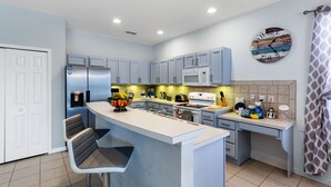 Uma cozinha moderna com uma ilha central, banquetas, micro-ondas e um relógio na parede.