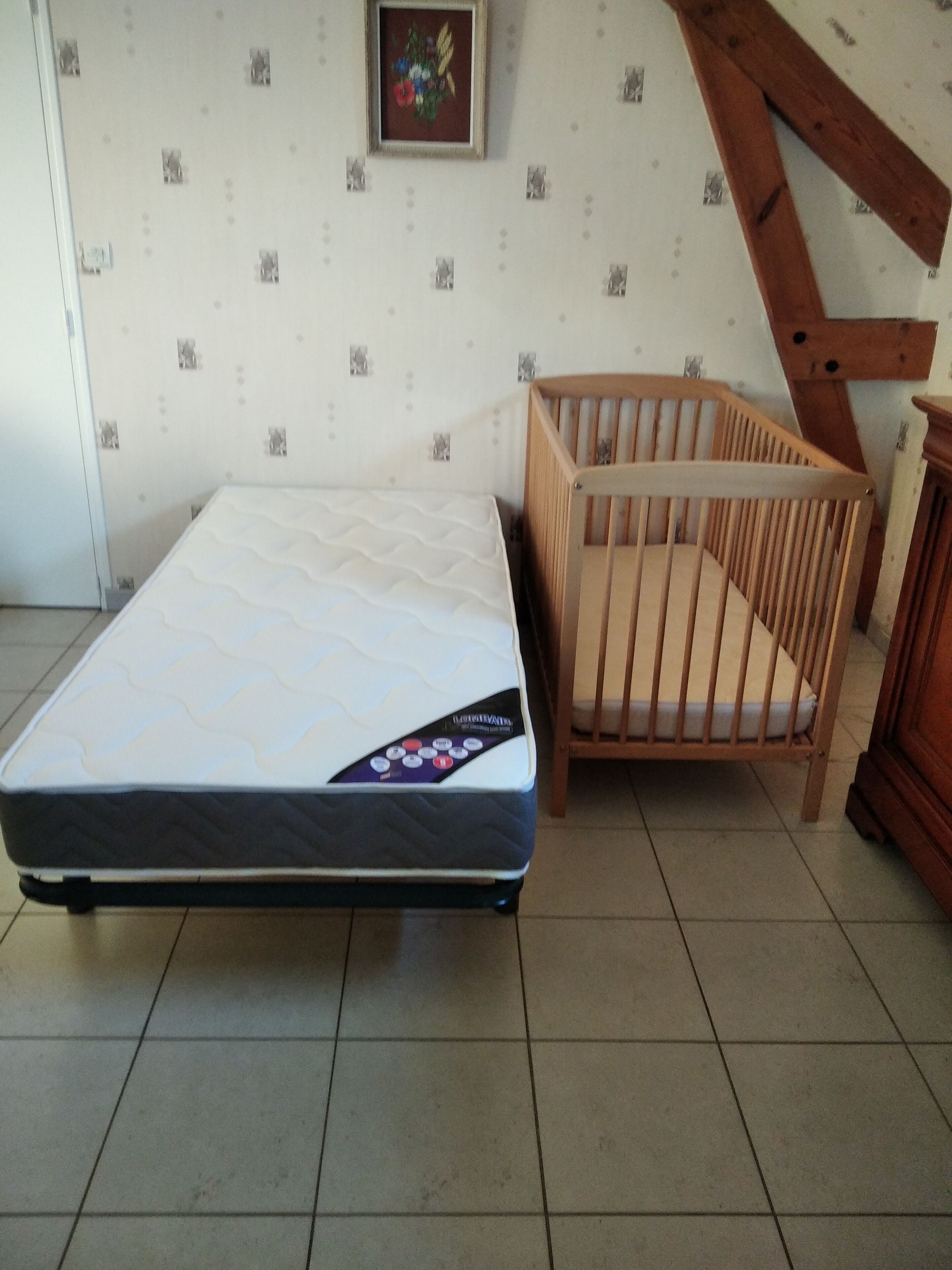 Une pièce avec un matelas, un berceau en bois et un mur orné d’un cadre de photo.