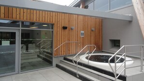 A modern building with a wooden exterior wall, a glass entrance, and a hot tub area with metal railings. - 7 km from DERVAL, stone house 4/5 adults + 1 baby. INTERNET BOX. (Conquereuil)
