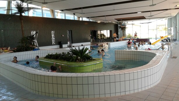 An indoor swimming pool with multiple lanes, a central island with plants, and a slide for children. - 7 km from DERVAL, stone house 4/5 adults + 1 baby. INTERNET BOX. (Conquereuil)