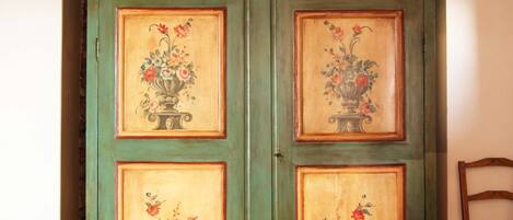 Un armario verde con diseños florales en las puertas, una pared de piedra arriba y una silla de madera a la derecha.