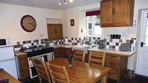 A kitchen with wooden cabinets, a dining table with chairs, a clock, and a stove.