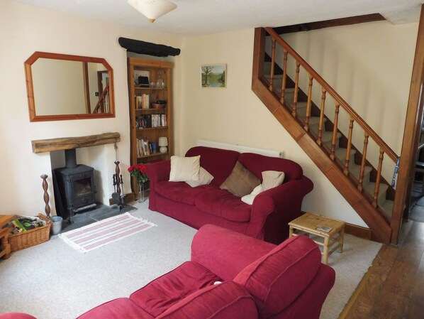A living room with a red sofa, a fireplace, a wooden staircase, and a bookshelf. - Traditional Grade 2 listed cottage. Quiet area of central Windermere. Log stove (Windermere, Cumbria)