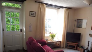 A living room with a red sofa, a television on a wooden stand, a window with curtains, and a door with a window.