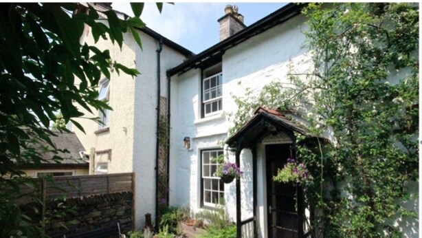 A quaint white building with a black door, surrounded by lush greenery and potted plants.
