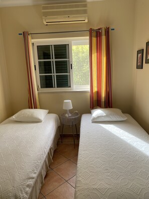 A room with two beds, a window with curtains, an air conditioner, and a small table with a lamp. - Algarve, Almancil: Fully secluded villa with private pool urb. Varandas do Lago. (Almancil)