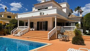 Una casa de dos pisos con piscina, zona de estar al aire libre y una escalera que lleva a la entrada.
