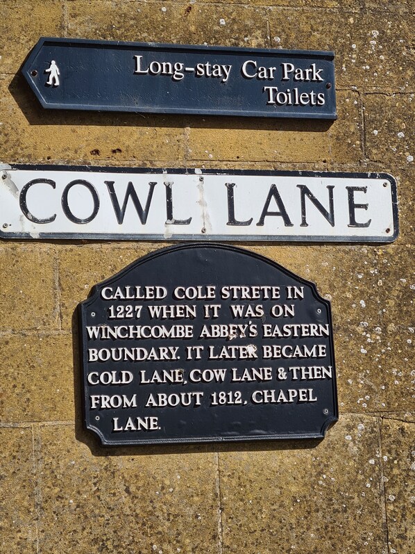 A street sign for 'COWL LANE' with historical information about its name changes and a sign for 'Long-stay Car Park Toilets'.