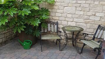 A patio with a stone wall, a large potted plant, a wooden bench, and a small round table.