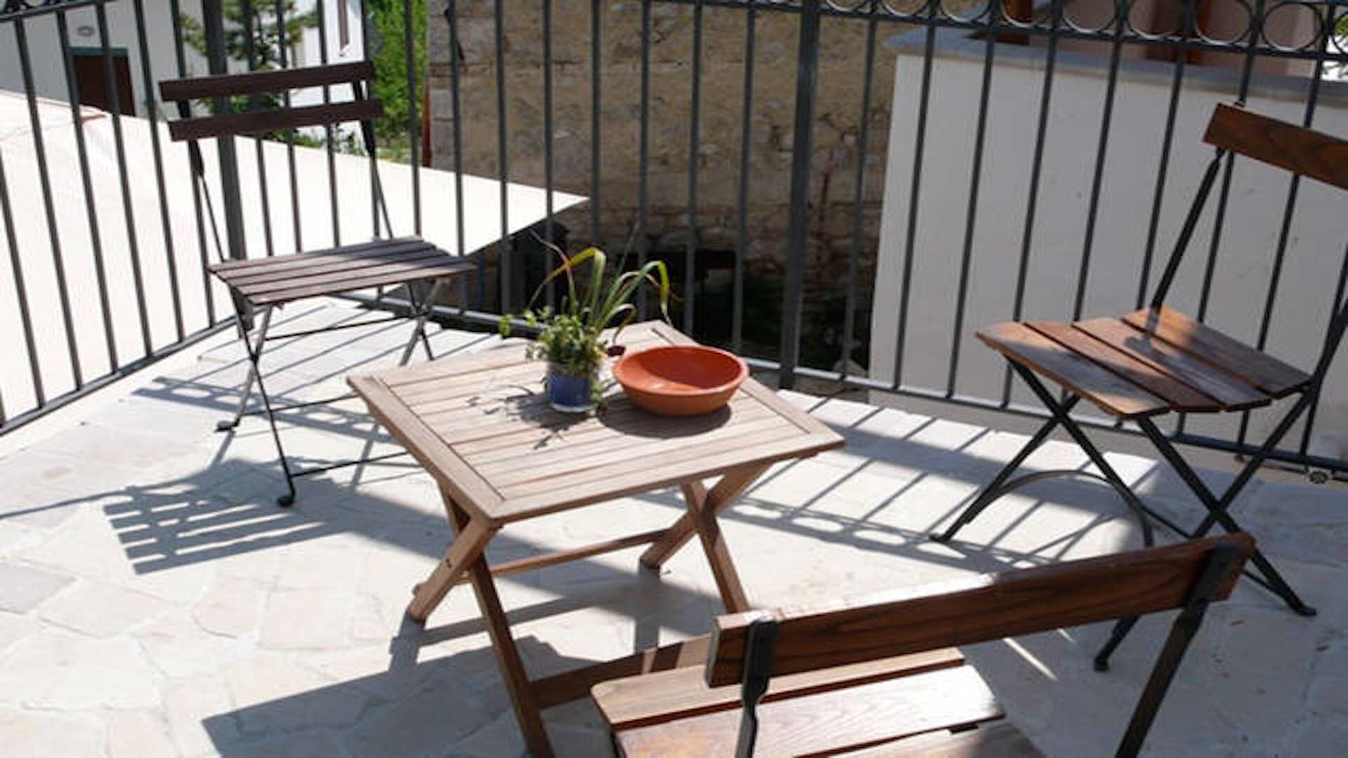 Een klein terras buiten met een houten tafel, twee stoelen en een plant in pot.