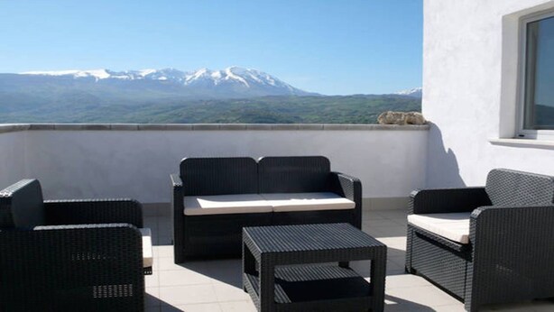 Ein Balkon mit Korbmöbeln, Blick auf einen Berg und eine weiße Wand.