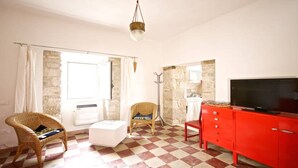Ein Zimmer mit Schachbrettfußboden, einem Korbsessel, einem weißen Pouf, einem roten Schrank und einem Fernseher.