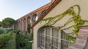 Un edificio de fachada de ladrillo y ventanas arqueadas, rodeado de exuberante vegetación y un jardín cuidado.