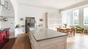 Een ruime keuken met een groot eiland, houten kastjes en een eethoek met een groene stoel.
