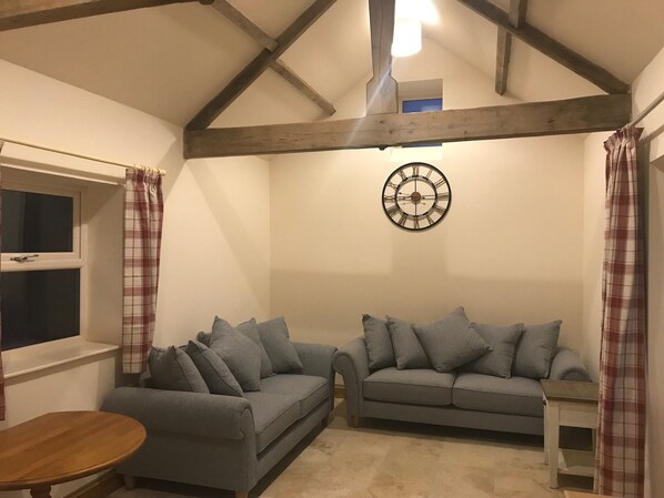 Une pièce chaleureuse avec deux canapés gris, une table en bois et une horloge décorative au mur.