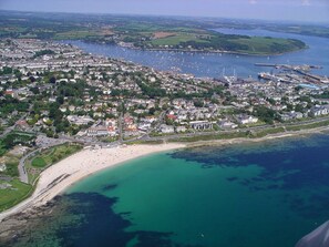 An aerial view of a coastal town with a sandy beach, a marina, and residential areas.