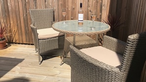 A wicker outdoor dining set with a glass table and chairs, a bottle of wine, and a glass on the table. - A comfortable well located property in Falmouth with generous parking (Falmouth)
