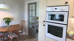 A kitchen with a double oven, wooden chairs, a dining table, and a vase of flowers. - A comfortable well located property in Falmouth with generous parking (Falmouth)