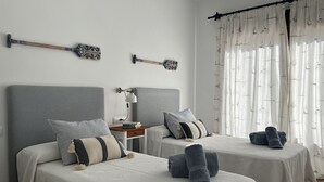 Una habitación de hotel con dos camas, una mesita de noche con lámpara y una ventana con cortinas.