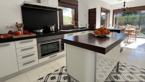 Una cocina moderna con una isla central, horno integrado y un comedor con vistas al exterior.