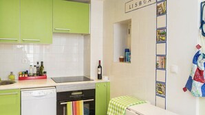 A compact kitchen with green cabinets, a dishwasher, an oven, and a refrigerator. A wine bottle is on the counter. - Castle / Alfama in the historic center (Lisboa)