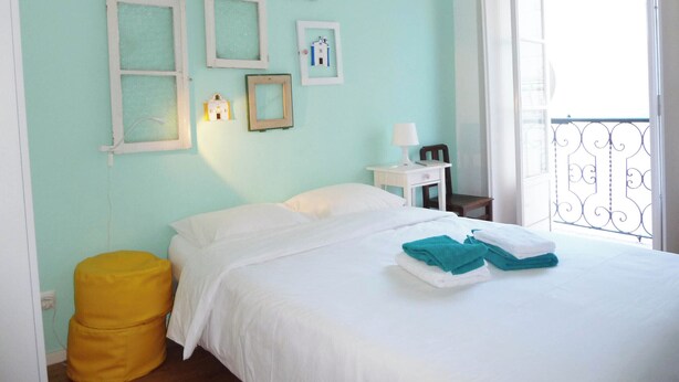 A bedroom with a bed, a nightstand, a lamp, and a window with a balcony. - Castle / Alfama in the historic center (Lisboa)