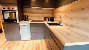 A compact kitchen with a dishwasher, a stove, a sink, and a coffee maker. - 2 bedroom apt, balcony facing Mont Blanc, very close to village & GM ski lift (Chamonix-Mont-Blanc)
