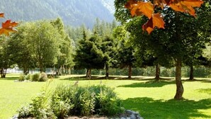 A serene park with a variety of trees, a small rock garden, and a lake in the background. - 2 bedroom apt, balcony facing Mont Blanc, very close to village & GM ski lift (Chamonix-Mont-Blanc)