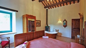 A bedroom with a large bed, wooden headboard, a wooden wardrobe, a mirror, a wall-mounted clock, and a window with a view. - Casale Vigneto - 3 bedrooms, pool, AC, wifi, pets, Marche (Mogliano)