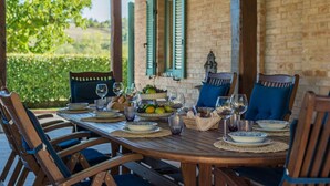 An outdoor dining area with a brick wall, green shutters, and a table set for four with plates, glasses, and a basket of fruits. - Casale Vigneto - 3 bedrooms, pool, AC, wifi, pets, Marche (Mogliano)