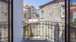 Ein Balkon mit Steinmauer und Metallgeländer, der auf eine enge Straße mit Gebäuden blickt.