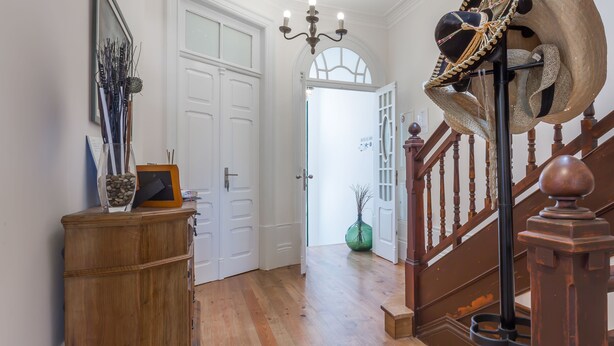 Ein Flur mit Holzboden, einer Kristallleuchter, einem Holzschrank und einer Treppe mit einer verzierten Kappe.