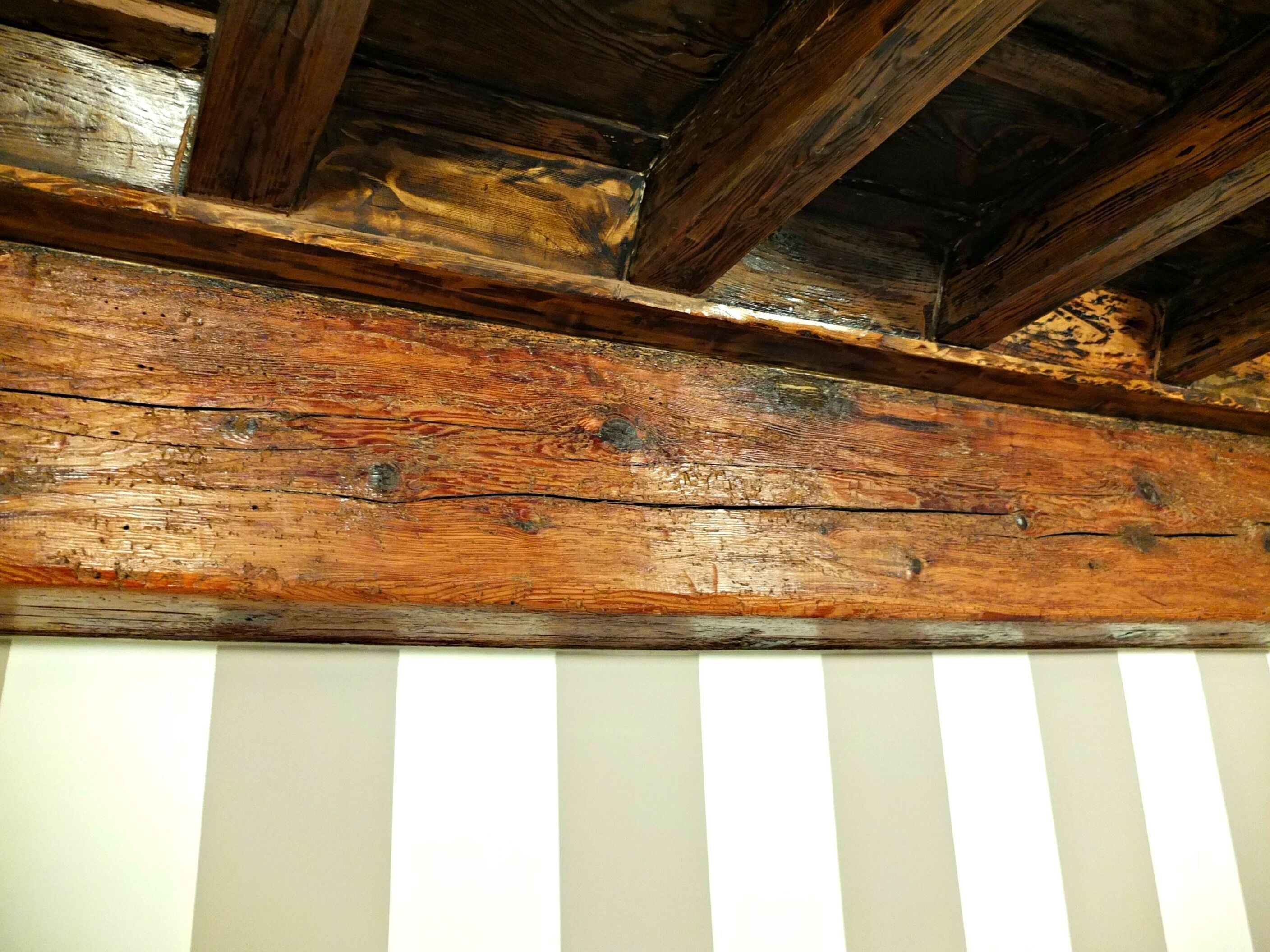 Una viga de madera con desgaste visible y una pared blanca a rayas debajo.