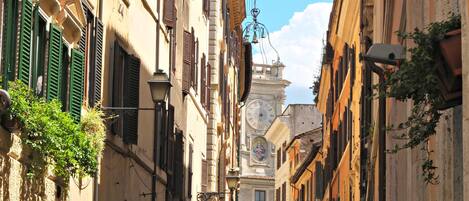 A narrow street lined with historic buildings, featuring a prominent clock tower in the background.