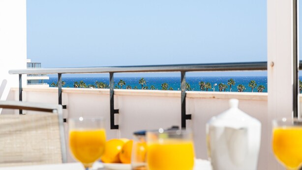 Ein Balkon mit Blick auf den Ozean, ein Tisch mit Orangensaftgläsern und eine weiße Kanne.