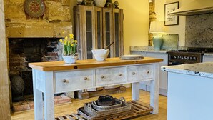 Una cocina con pared de piedra rústica, una mesa de madera con cajones, una chimenea de piedra y una estufa moderna.