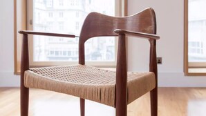 Une chaise en bois, dotée d’un siège et d’un dossier en osier, placée dans une pièce avec de grandes fenêtres donnant sur des bâtiments.