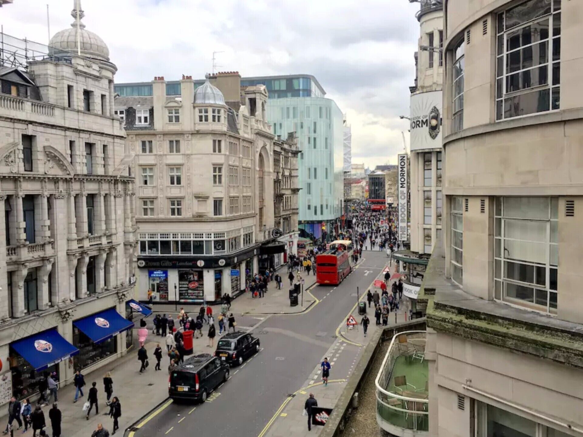 A busy urban street with historic buildings, a red double-decker bus, and pedestrians.