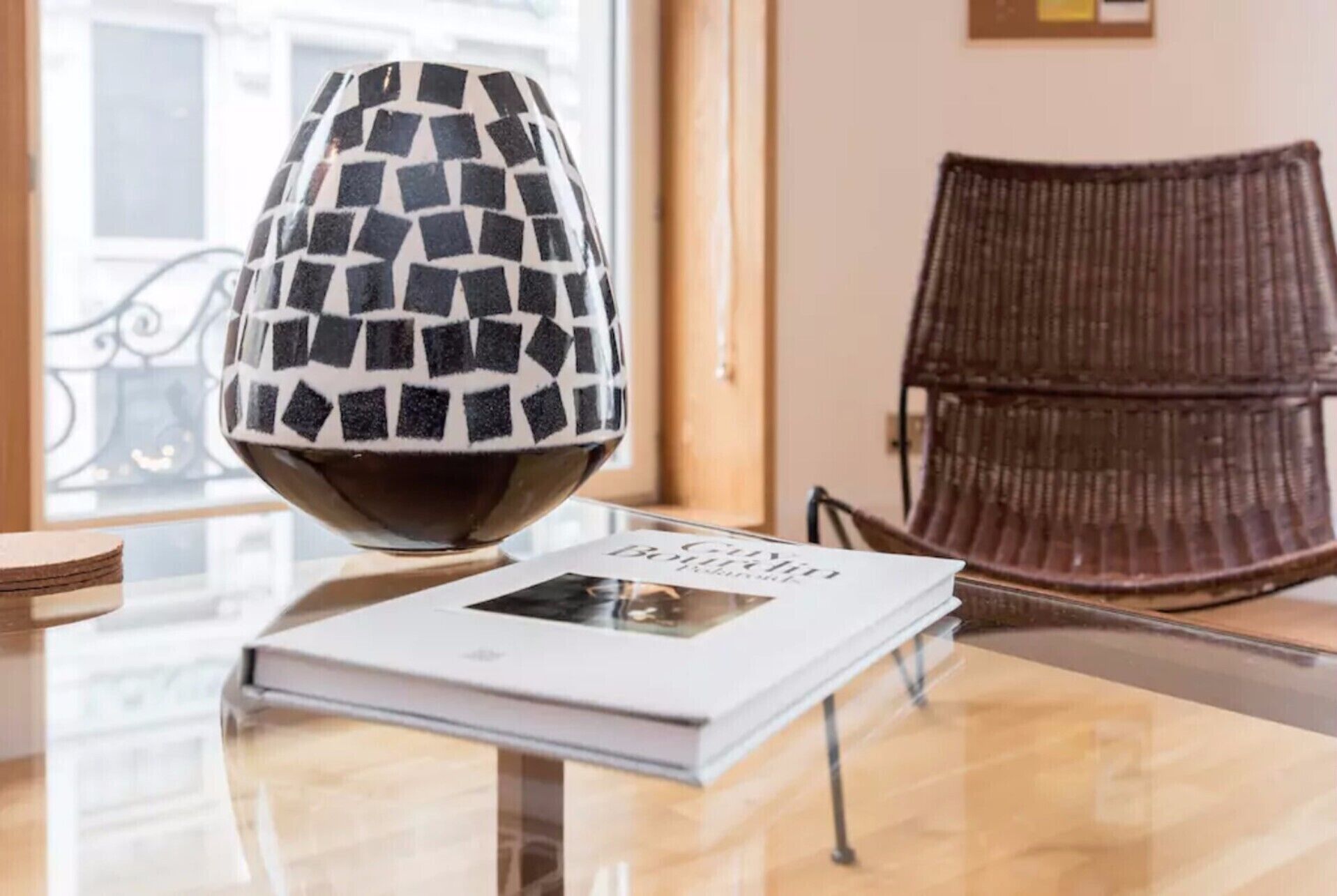 A book titled "CINEMA" on a glass table with a decorative lamp and a wicker chair in the background.