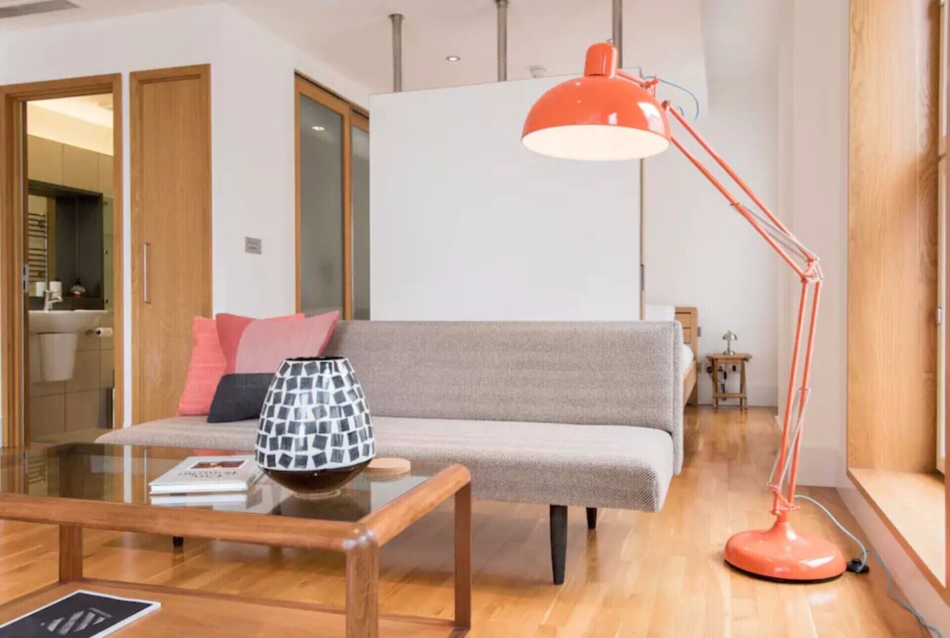 Een moderne woonkamer met een grijze bank, een glazen salontafel en een rode vloerlamp.