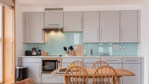Une cuisine moderne avec des meubles de couleur gris clair, une hotte en acier inoxydable et un coin repas comprenant une table et des chaises en bois.