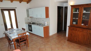 Une cuisine compacte avec des meubles blancs, une table à manger pour quatre personnes et un buffet en bois doté de portes en verre.