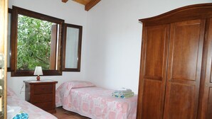 Une chambre avec deux lits, une armoire en bois, une table de chevet avec une lampe et une fenêtre donnant sur un paysage verdoyant.